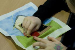 Small hands sewing a quilt square with a picture of a detached house