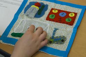 Small hand sewing a quilt square with a picture of the school playground
